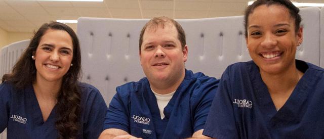 Three smiling healthcare professionals wearing scrubs with 威尼斯游戏大厅's logo displayed.